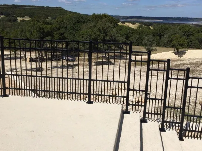 Black ornamental iron rail on a concrete patio with a lake view behind it