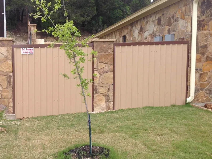 Tan metal privacy fence between stone pillars, with an A-1 Fence sign on the post